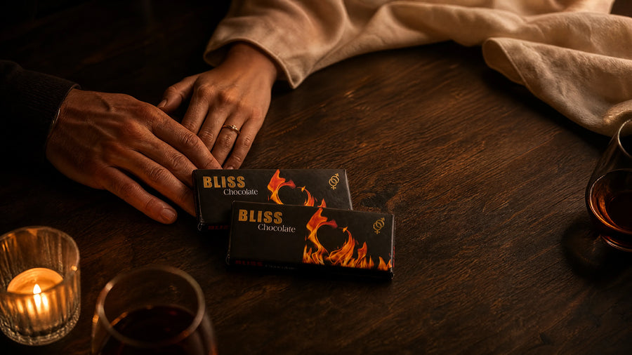 Two people's hands resting together by candlelight beside two Bliss Chocolate bars.